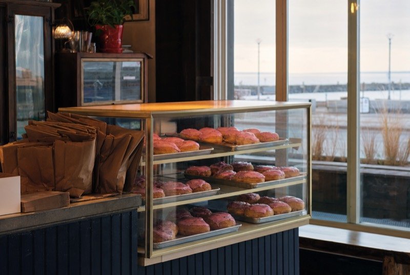A bakery display case with trays of round sweet pastries under pink icing