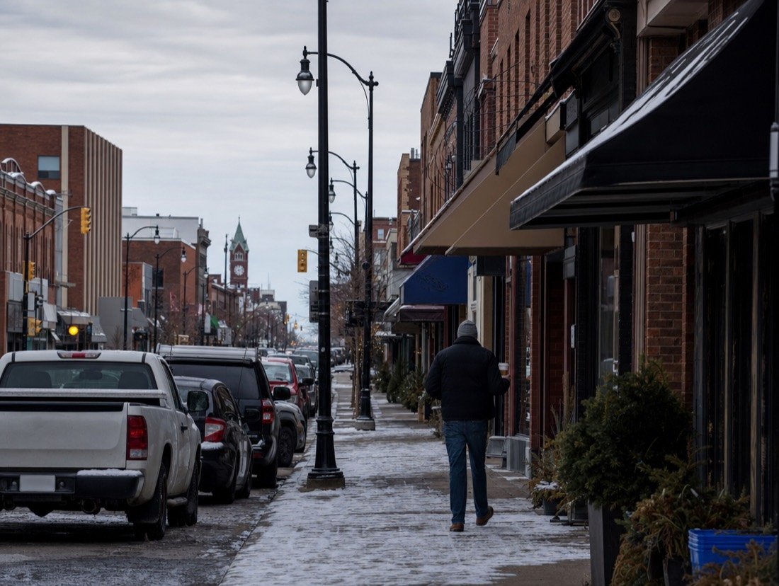 Two- and three-storey red-brick shopfronts with awnings and parked pickups after the first light snow