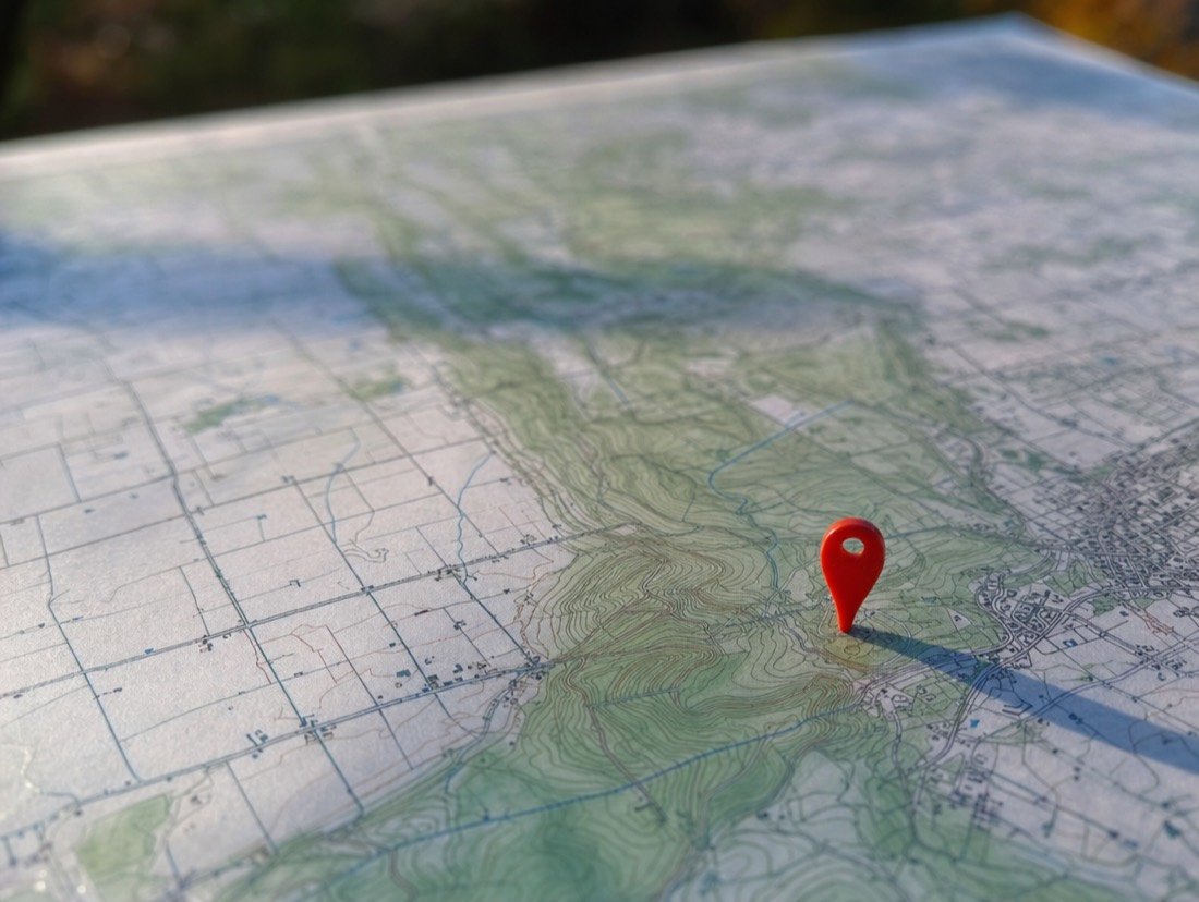 Close view of a red map pin stuck in contour lines on a paper map