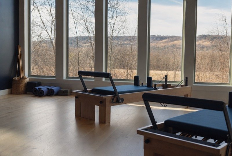 Reformer machines and rolled mats on a wooden studio floor lit by morning sun